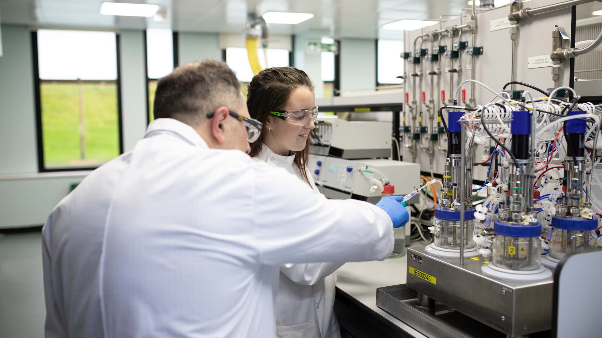 Two of our people in a lab at CPI's Wilton Centre wearing lab coats and googles inspecting a piece of equipment. Two of our people in a lab at CPI's Wilton Centre wearing lab coats and googles inspecting a piece of equipment.