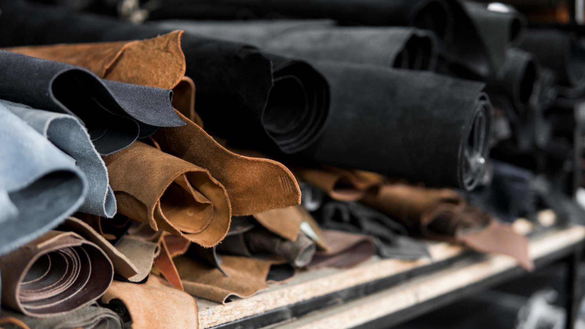 A photo showing rolled up leather, of different colours - blue, brown and black, on a shelf A photo showing rolled up leather, of different colours - blue, brown and black, on a shelf