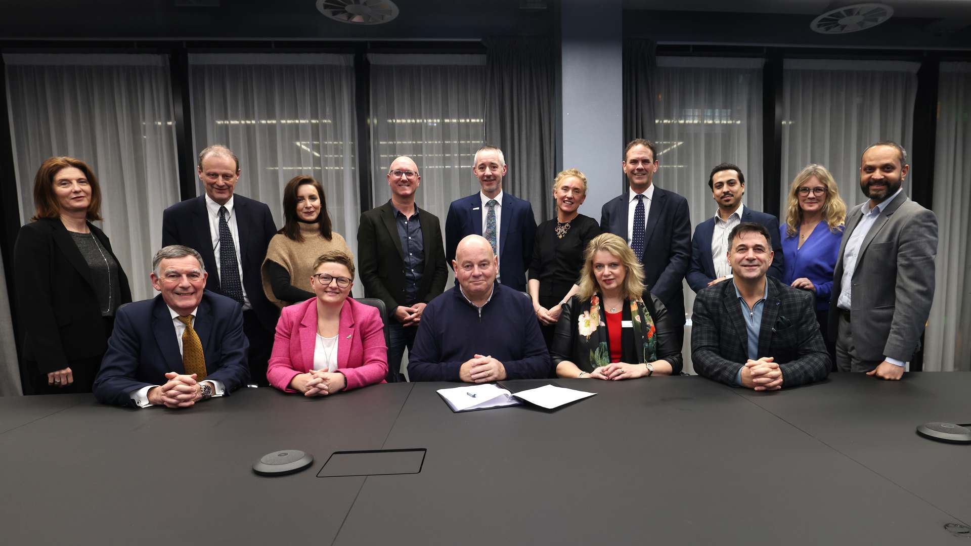 A photo of group of people from HVM Catapult, CPI, Greater Manchester Combined Authority, Bruntwood SciTech, and Innovation Greater Manchester, sitting and standing around a black table smiling at the camera after signing the MoU that is placed on the table in front of them. A photo of group of people from HVM Catapult, CPI, Greater Manchester Combined Authority, Bruntwood SciTech, and Innovation Greater Manchester, sitting and standing around a black table smiling at the camera after signing the MoU that is placed on the table in front of them.