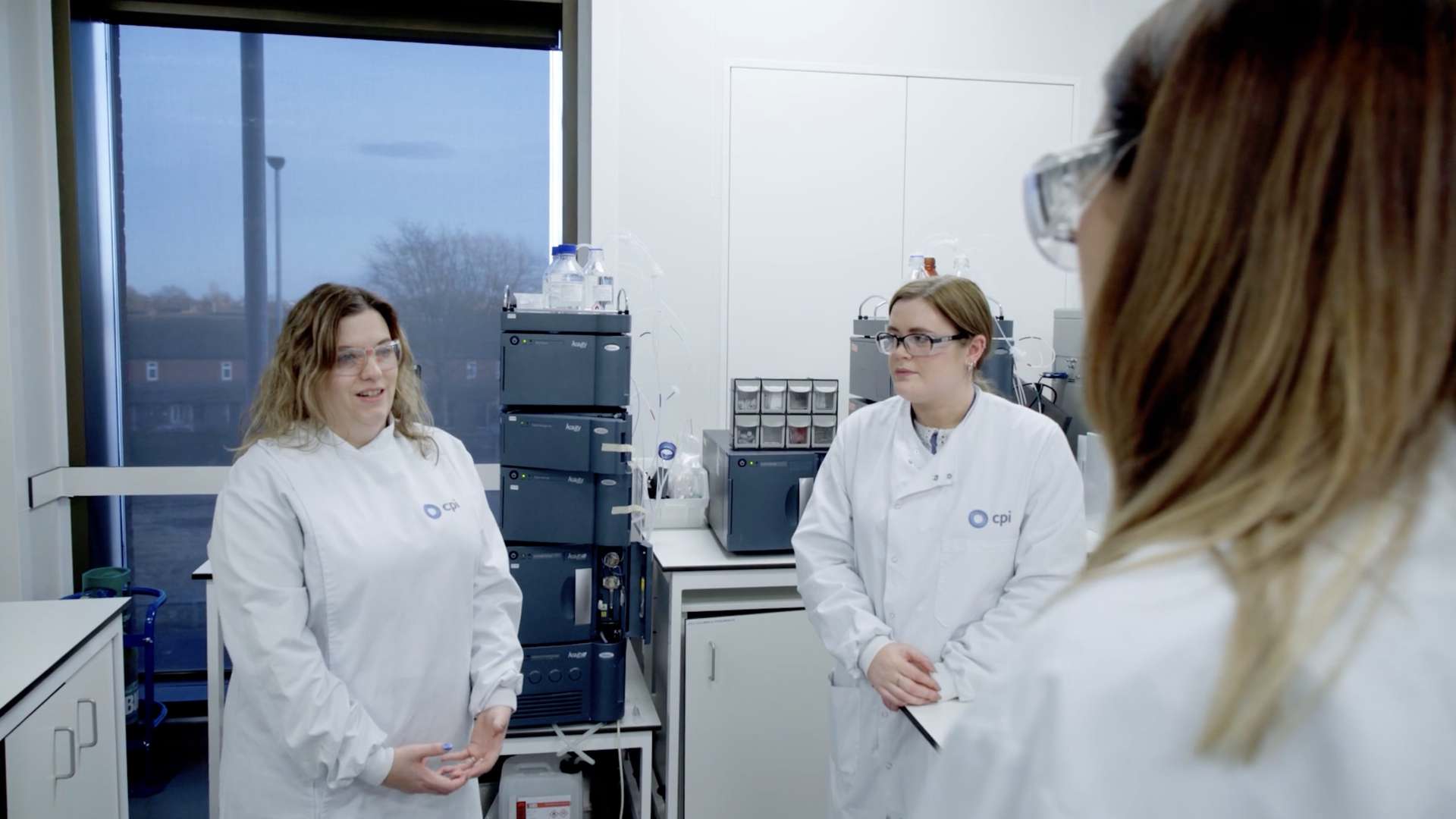 Three females in lab coats and goggles talking to each other in one of CPI's labs. Three females in lab coats and goggles talking to each other in one of CPI's labs.
