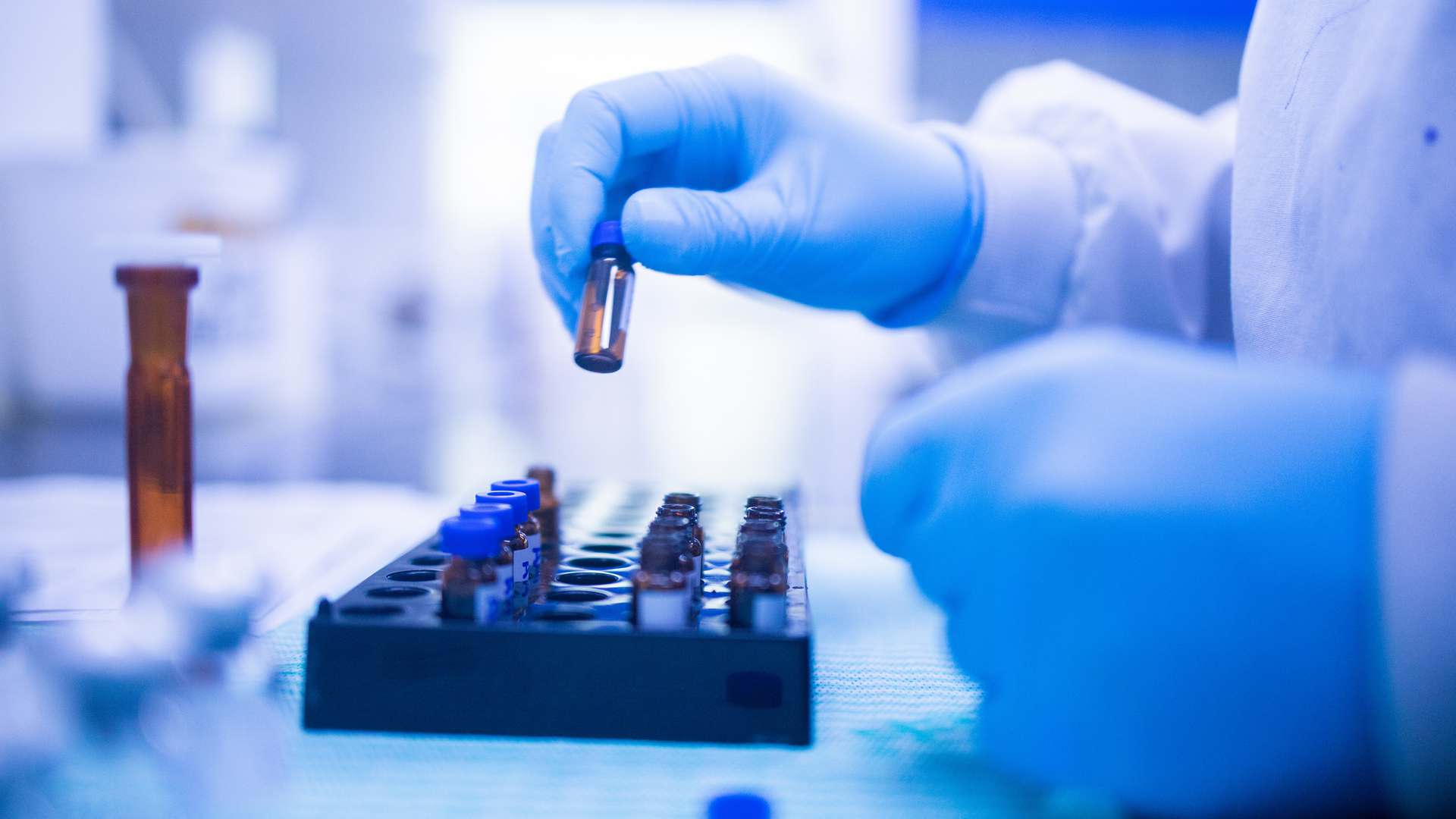 Hand with blue gloves adding vials to a tray. Hand with blue gloves adding vials to a tray.