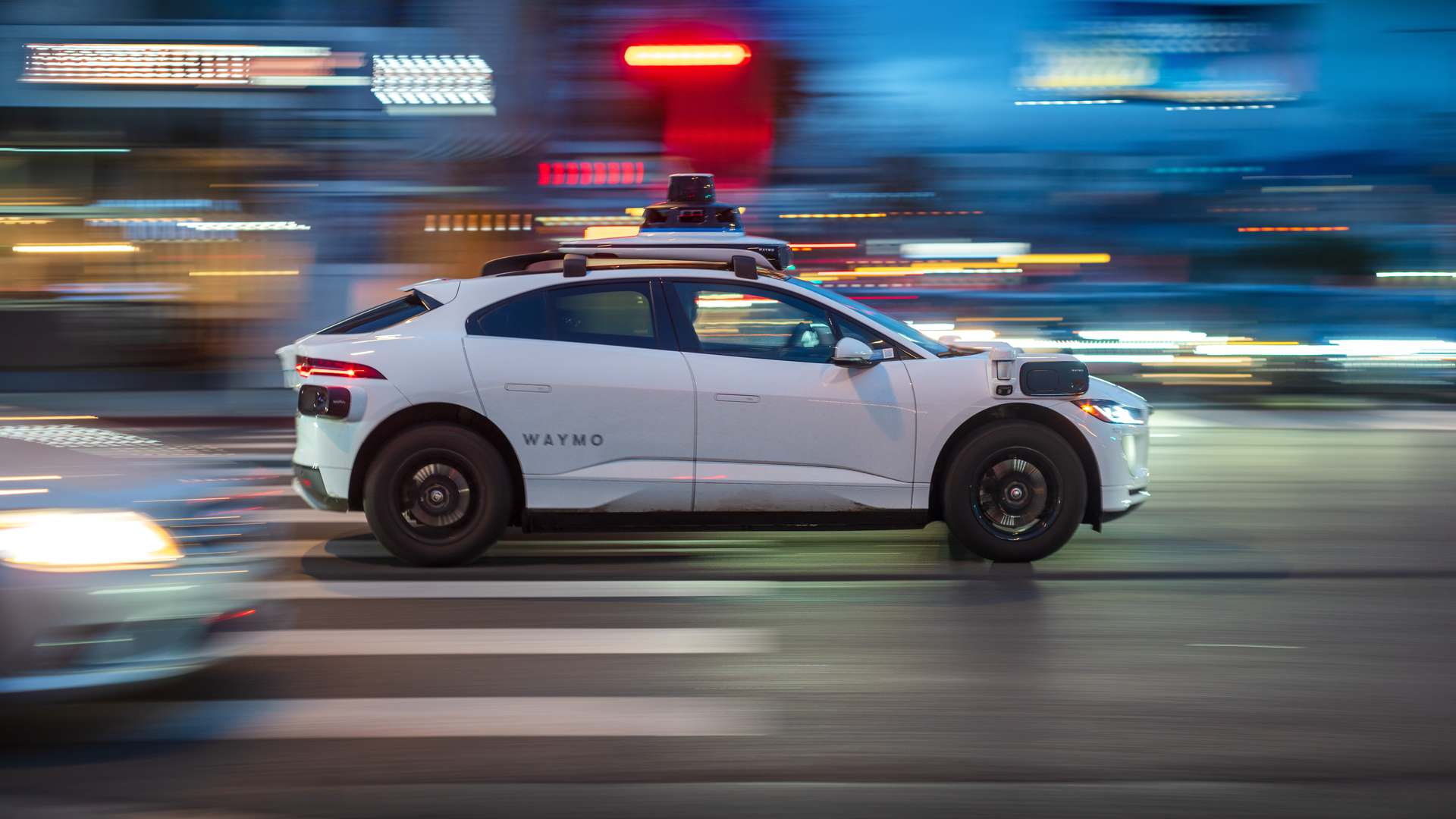 Waymo driverless taxi travelling through a busy city intersection at dusk, with illuminated streets and surrounding traffic in West Hollywood. Waymo driverless taxi travelling through a busy city intersection at dusk, with illuminated streets and surrounding traffic in West Hollywood.