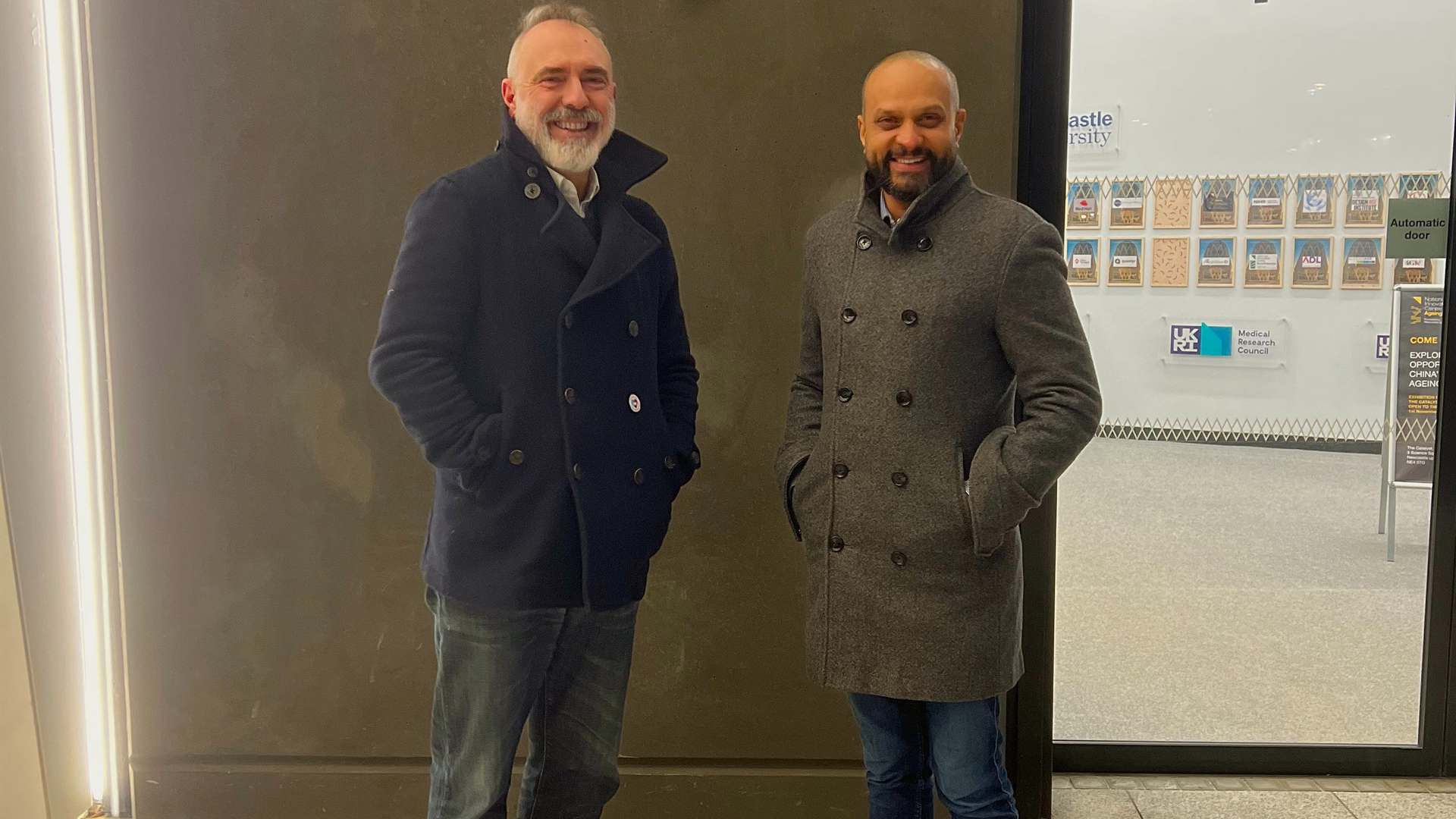 This is a photo of two men standing outside 'The Catalyst' building, the name is on the wall behind the men. This is a photo of two men standing outside 'The Catalyst' building, the name is on the wall behind the men.